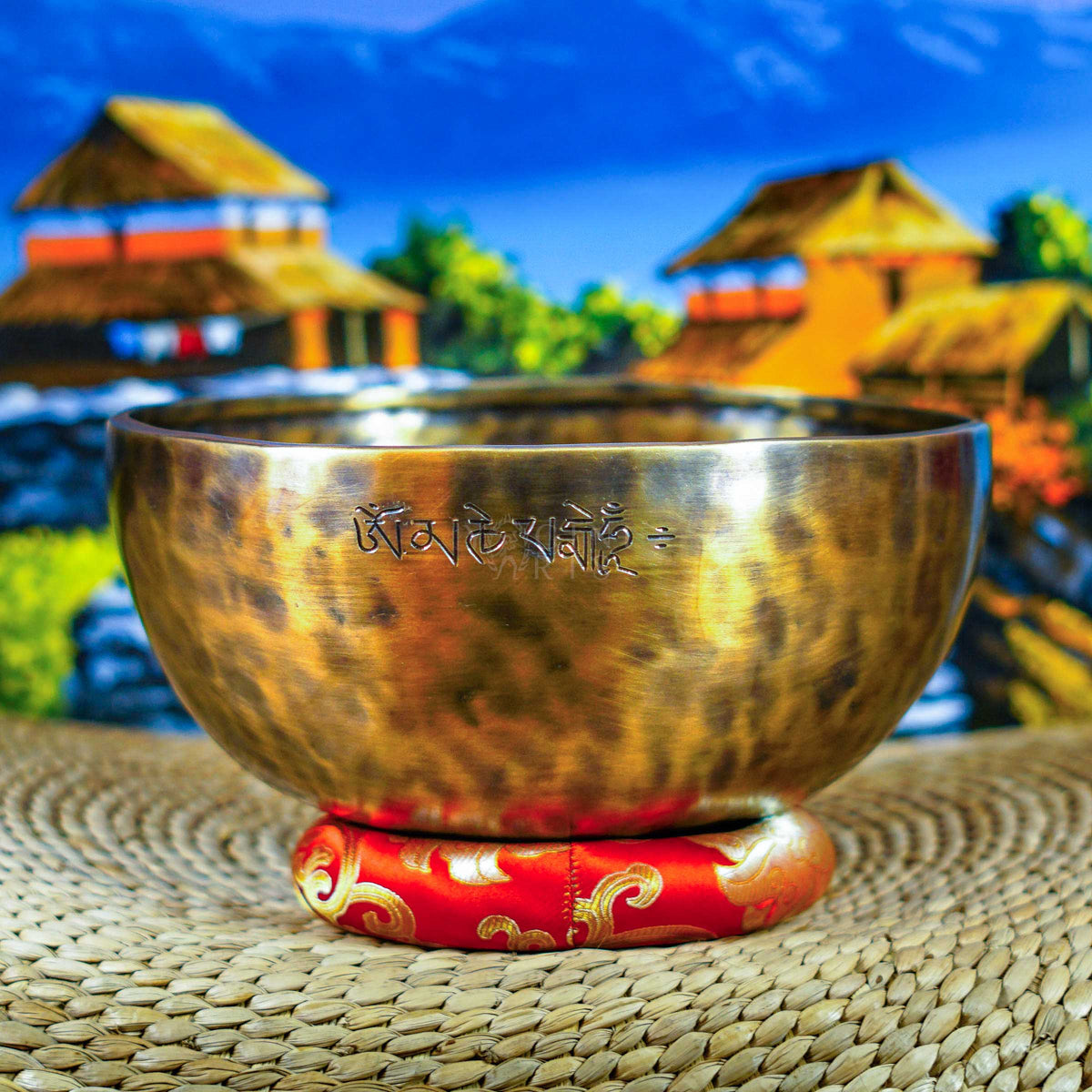 Side view of a handcrafted Himalayan singing bowl with warm bronze-gold finish, engraved Tibetan-style inscription and red decorative cushion.
