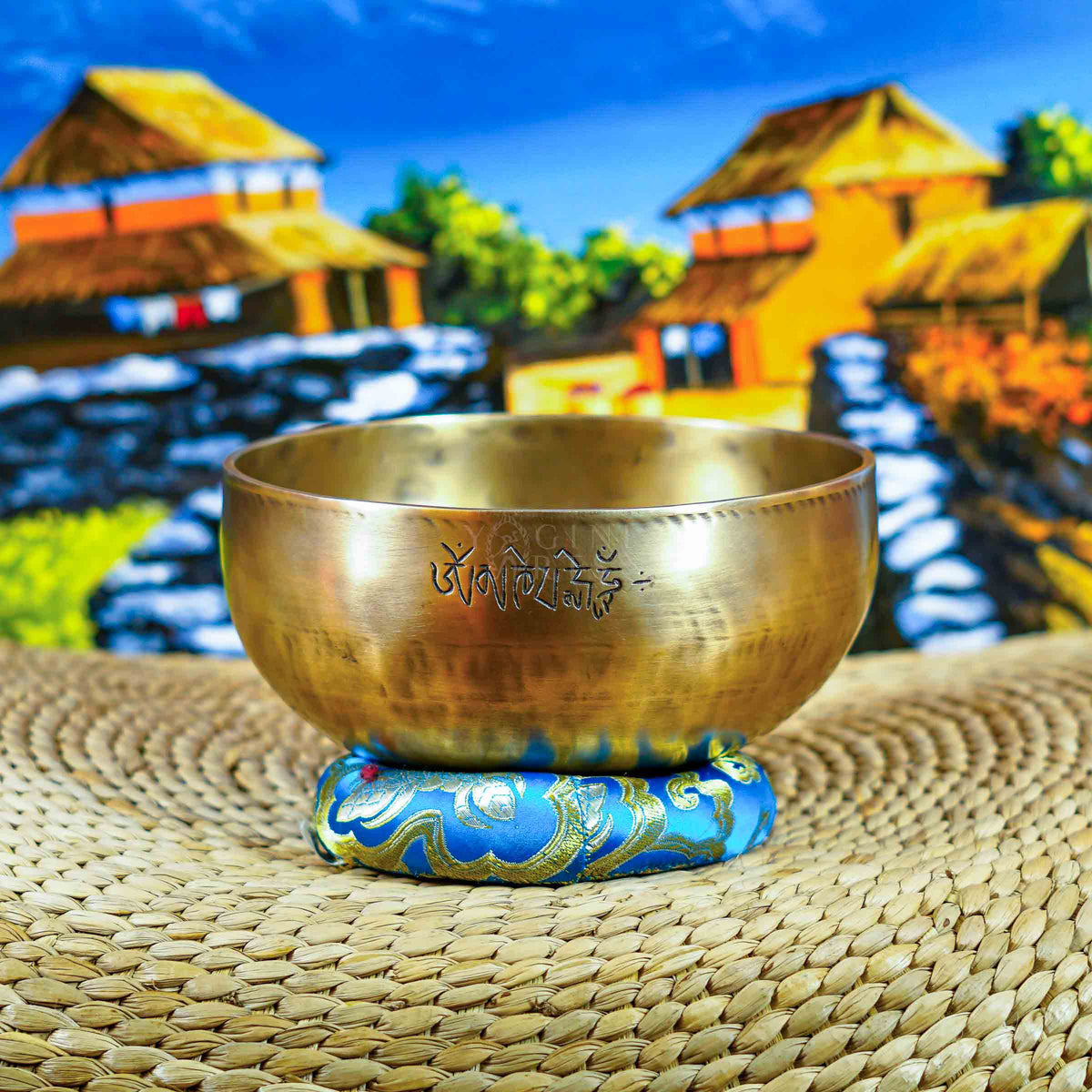 Front view of a handcrafted singing bowl with Om symbol, warm bronze finish, blue patterned cushion, and traditional wooden mallet.