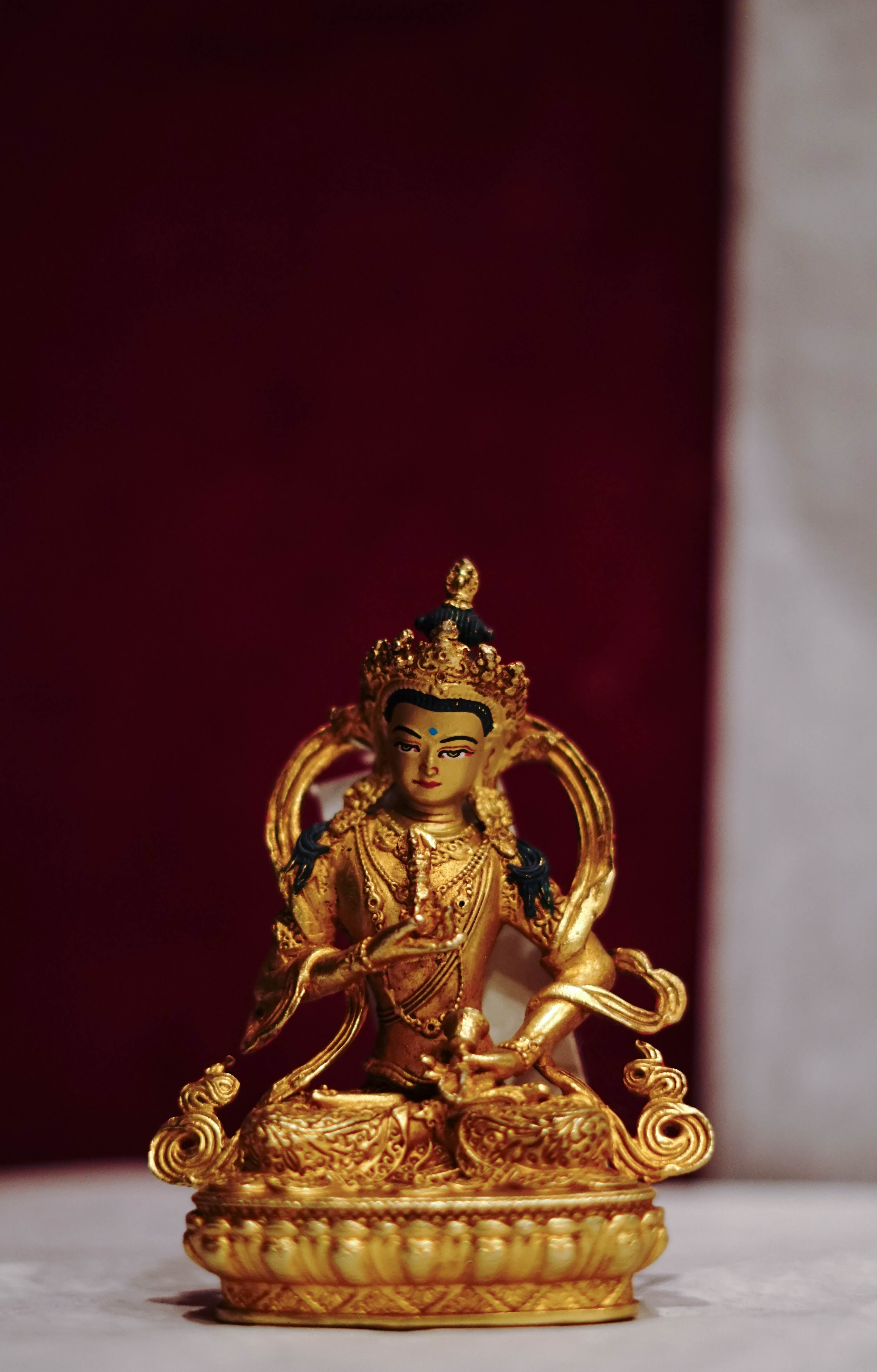 Golden statue of a seated Buddhist deity with intricate detailing, displayed on a plain background.