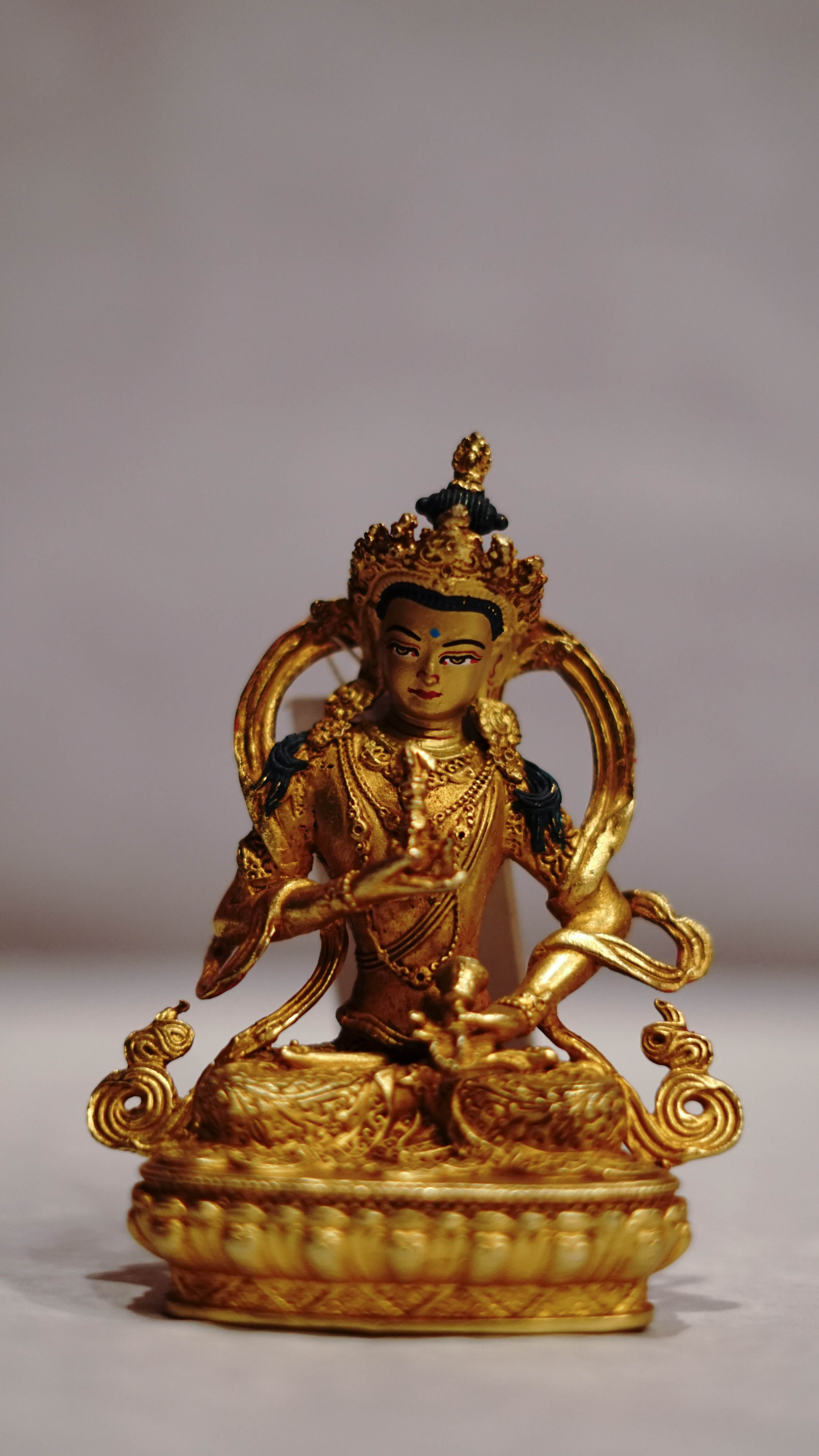 Golden statue of a seated Buddhist deity with intricate detailing, displayed on a plain background.