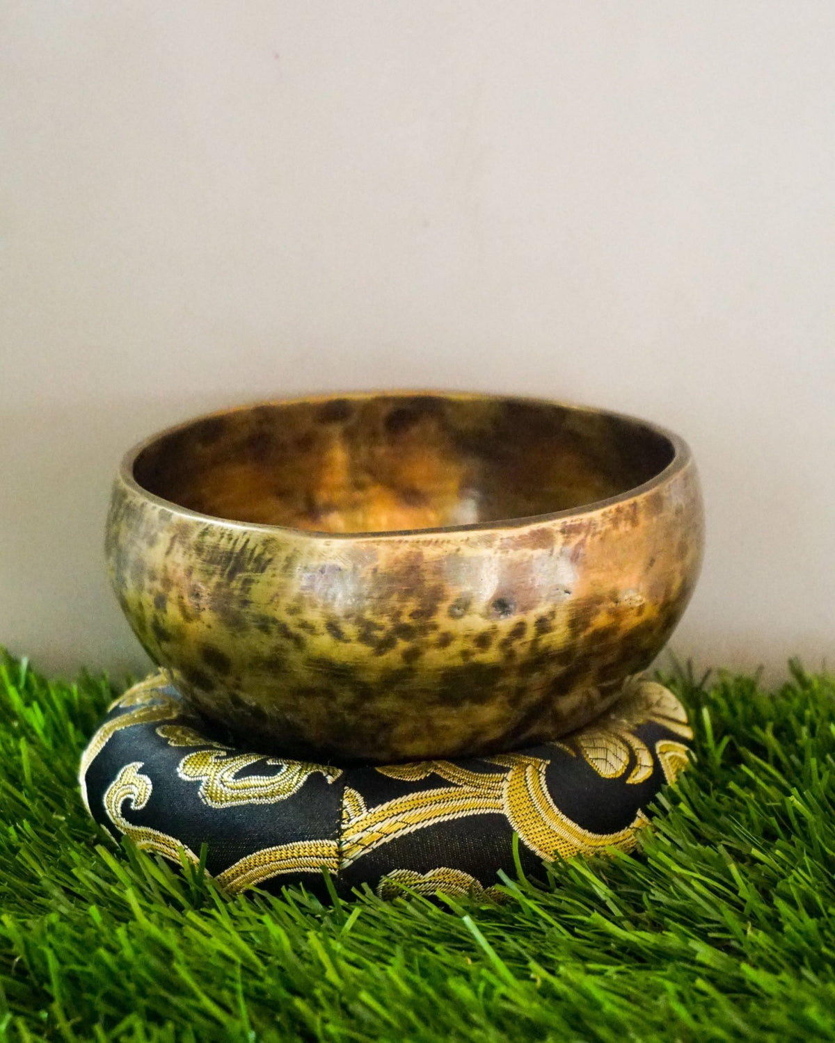 Brass singing bowl on a decorative pillow with a grassy background