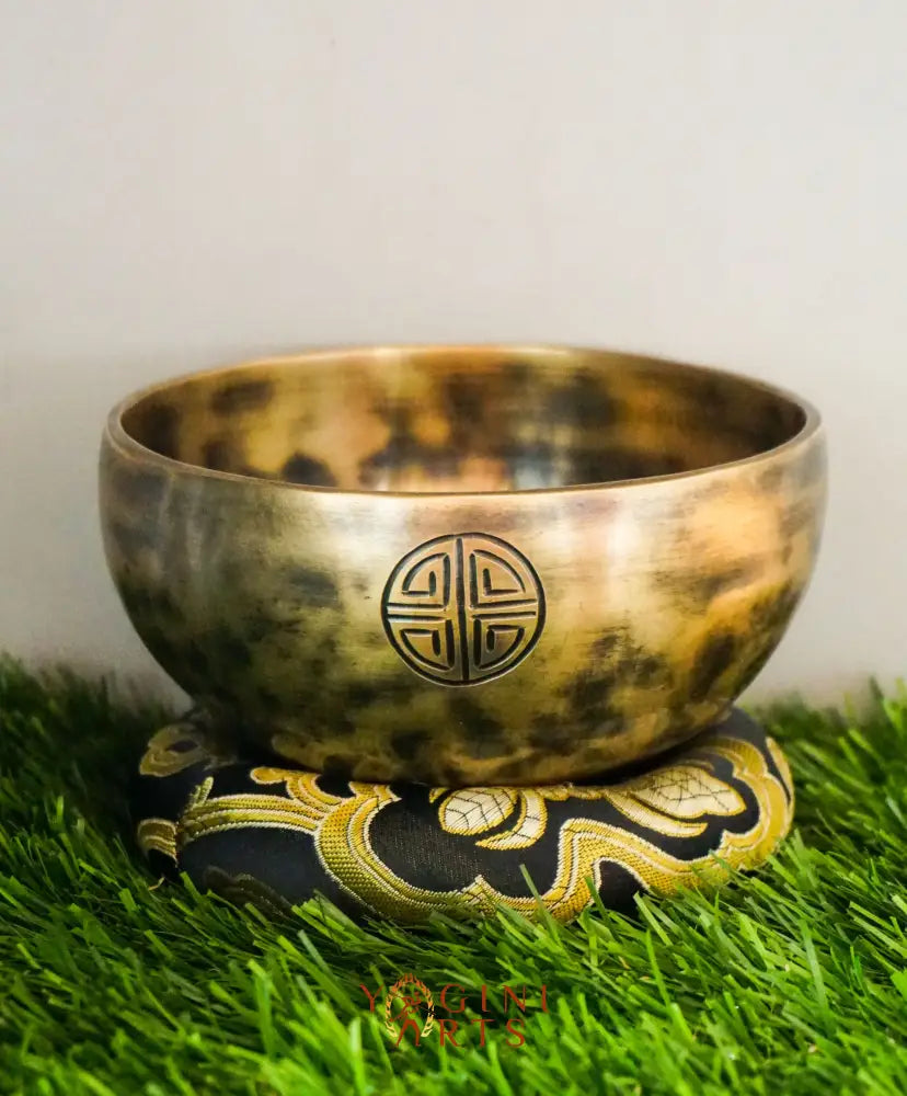Bronze singing bowl with a decorative emblem on a green grass-like surface