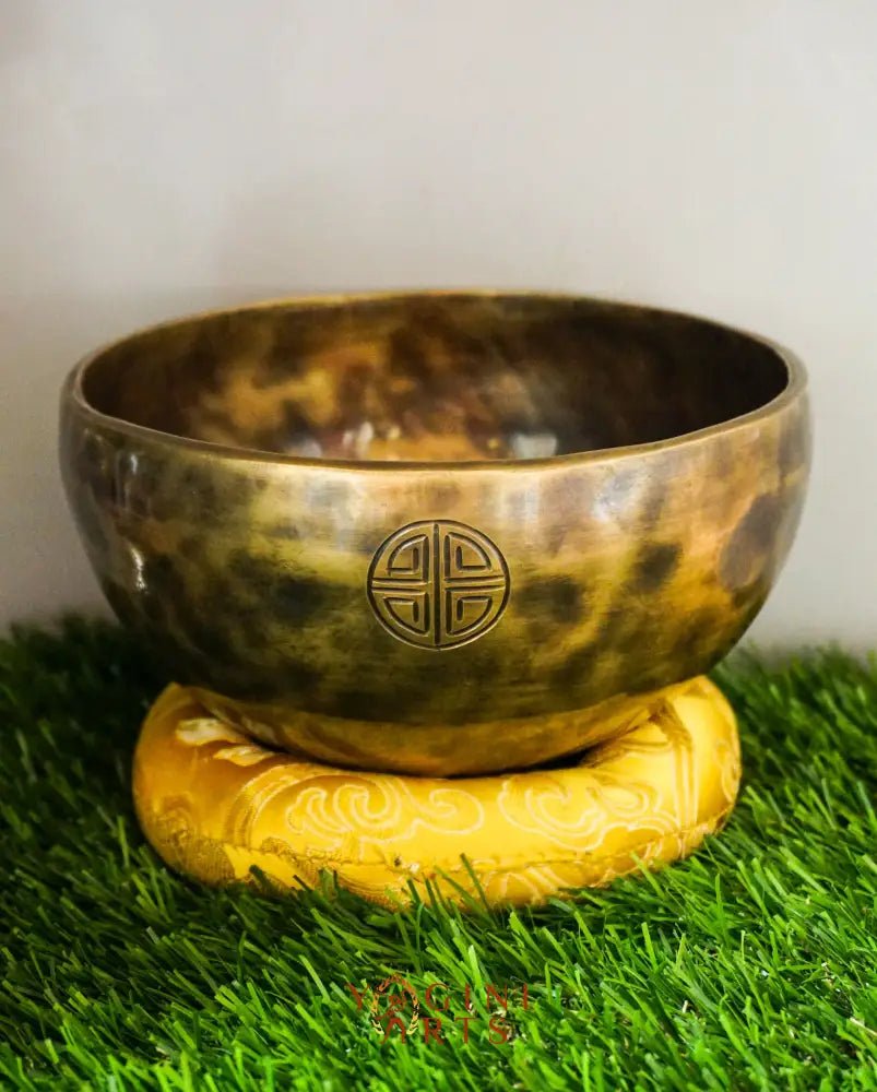 Bronze singing bowl with emblem on a yellow stand on green grass
