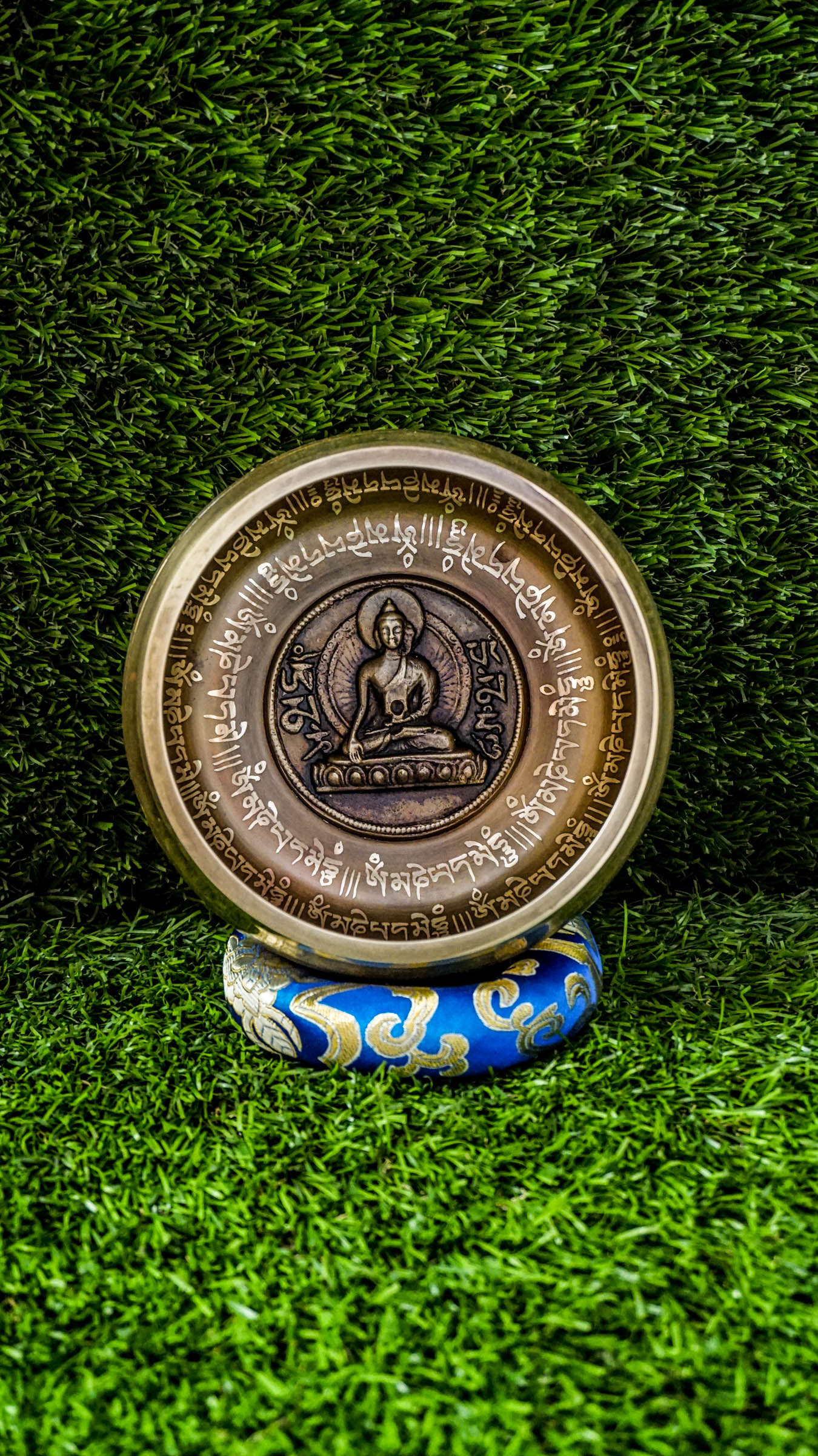 Bronze singing bowl with a carved meditating Buddha at the center, surrounded by the Om Mani Padme Hum mantra inside and engraved again around the outside, radiating peaceful, grounding energy.