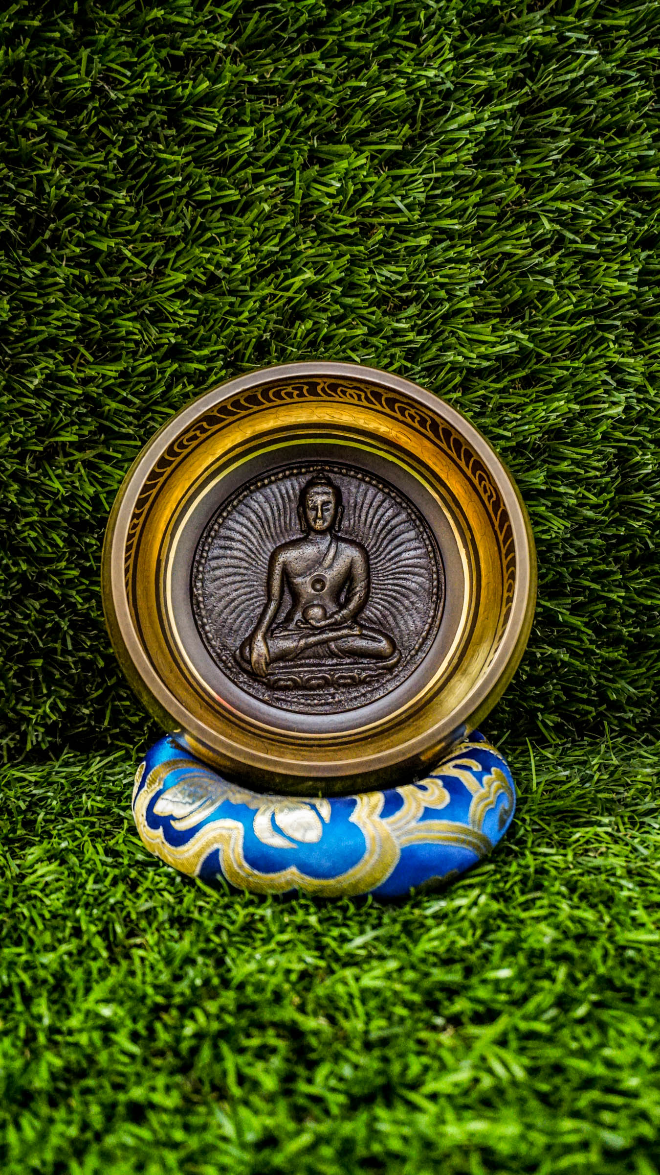 Singing bowl with a carved meditating Buddha inside and "Om Mani Padme Hum" mantra in a floral design on the outside.