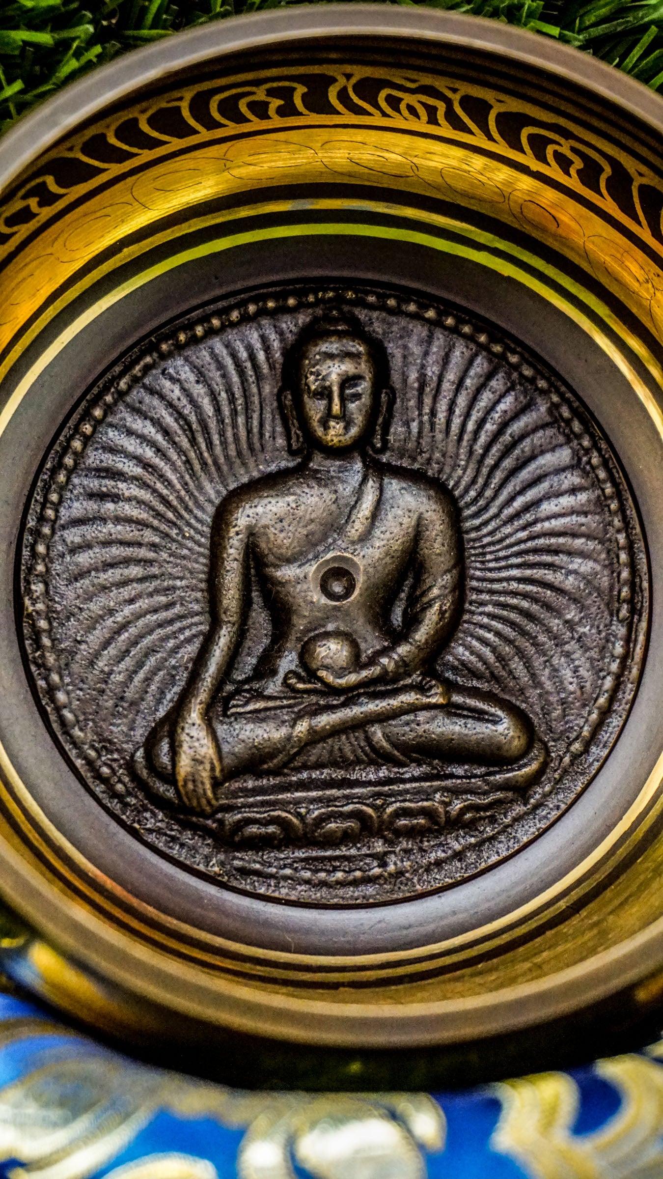 Singing bowl with a carved meditating Buddha inside and "Om Mani Padme Hum" mantra in a floral design on the outside.