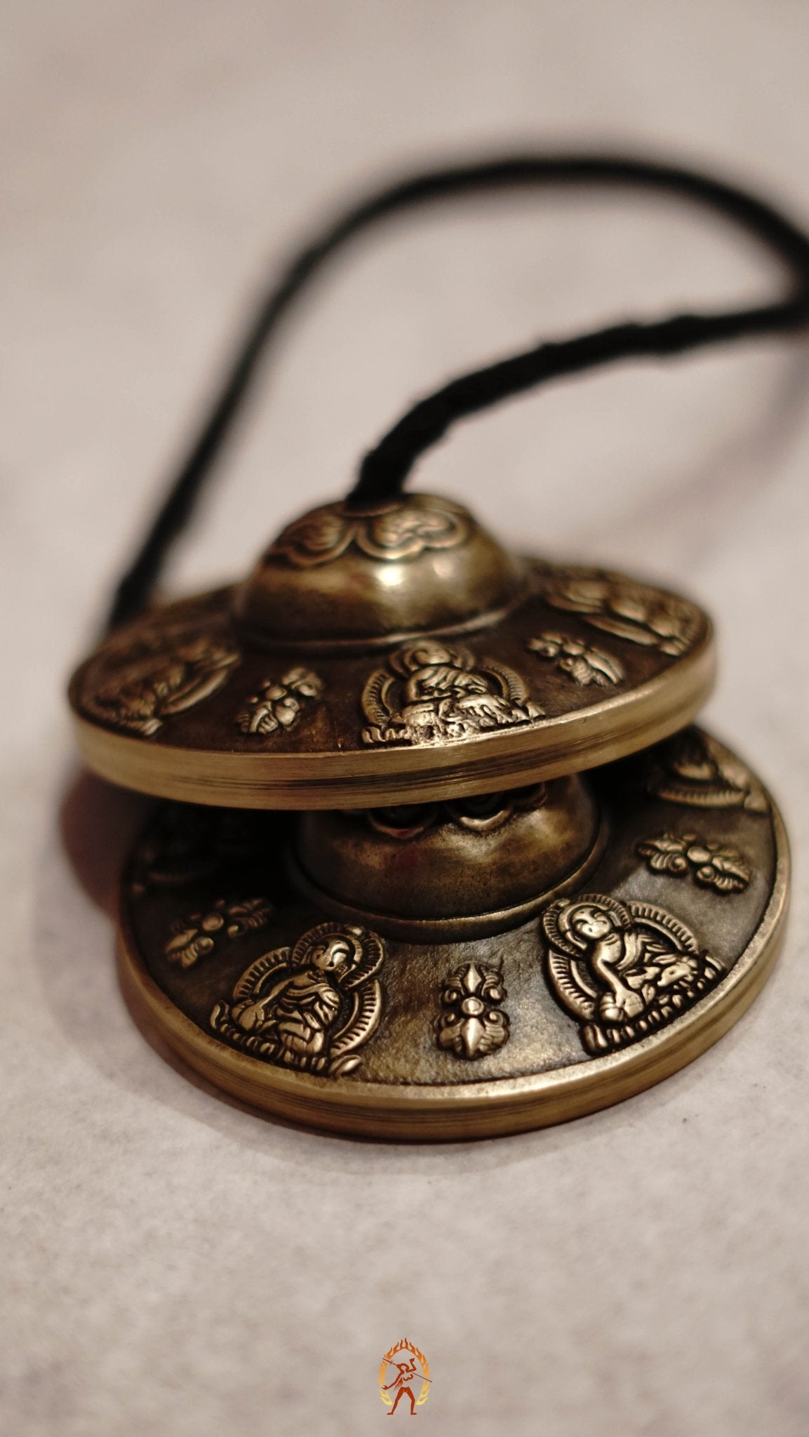 Close-up of bronze tingsha meditation cymbals with detailed Buddhist engravings, resting on a gray textured surface.