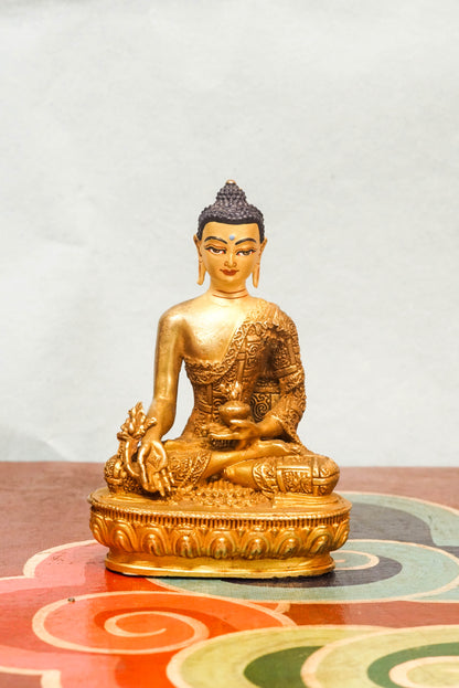 Handcrafted Medicine Buddha statue with open eyes, holding a healing bowl and medicinal plant, surrounded by a radiant lapis blue aura, seated on a lotus pedestal.