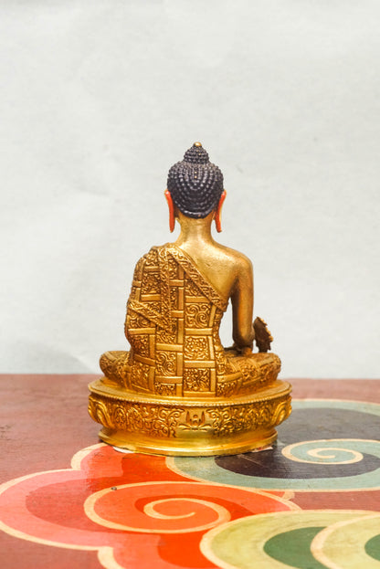 Handcrafted Medicine Buddha statue with open eyes, holding a healing bowl and medicinal plant, surrounded by a radiant lapis blue aura, seated on a lotus pedestal.