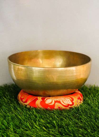 Handmade brass Tibetan singing bowl on a red cushion for sound healing.