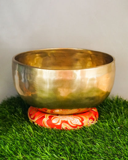 Handmade brass Tibetan singing bowl on a red cushion for sound healing.