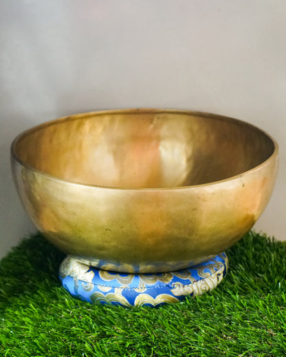 Handmade brass Tibetan singing bowl on a red cushion for sound healing.