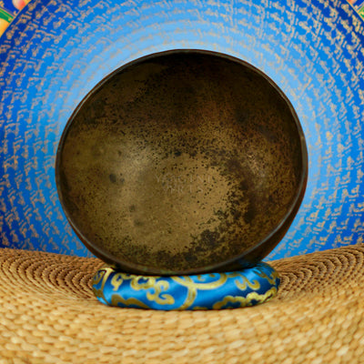 Semi antique Tibetan singing bowl handmade in Nepal with aged bronze finish on a traditional blue cushion