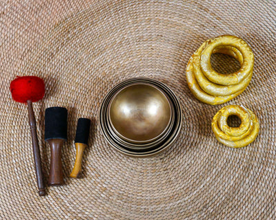 Seven handcrafted Himalayan-style singing bowls arranged in a circular formation, showing graduated sizes and warm antique bronze-gold finishes.