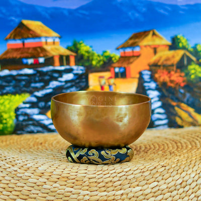 Handcrafted Himalayan singing bowl with a warm bronze-gold finish displayed on a decorative blue cushion for meditation practice.
