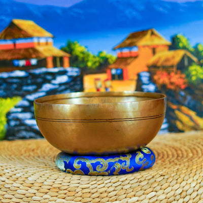 Handcrafted Himalayan singing bowl with a warm bronze-gold finish displayed on a decorative blue cushion for meditation practice.