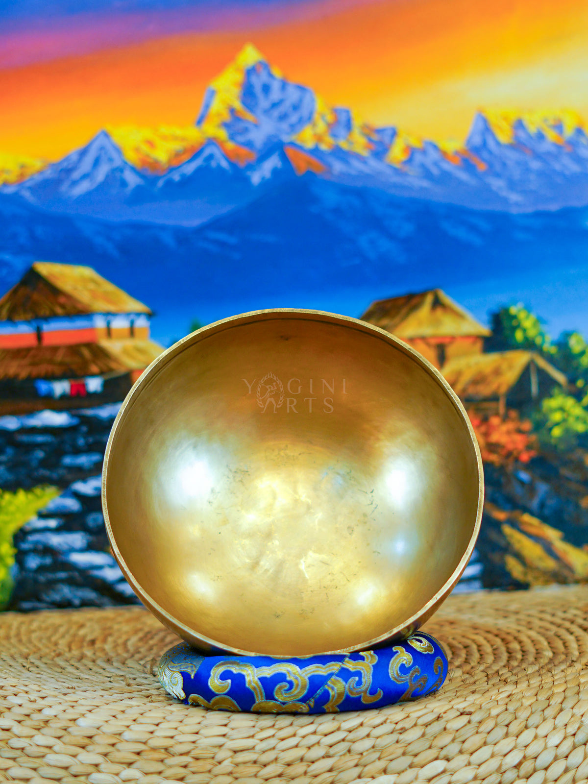 Front view of a handmade bronze-gold singing bowl showing its smooth metal surface and rounded form on a patterned cushion.