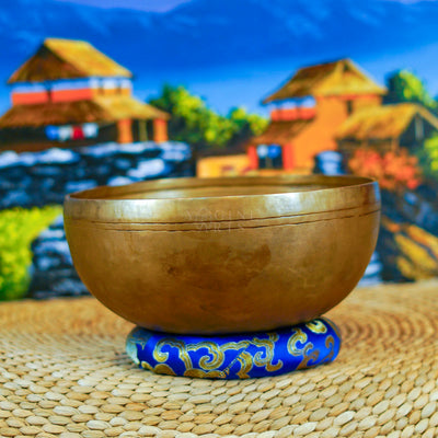 Handcrafted Himalayan singing bowl with a warm bronze-gold finish displayed on a decorative blue cushion for meditation practice.