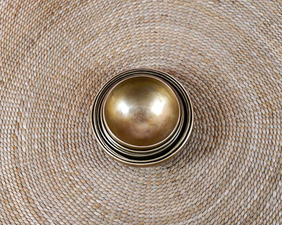 Seven handcrafted Himalayan-style singing bowls arranged in a circular formation, showing graduated sizes and warm antique bronze-gold finishes.