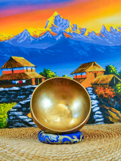 Front view of a handmade bronze-gold singing bowl showing its smooth metal surface and rounded form on a patterned cushion.