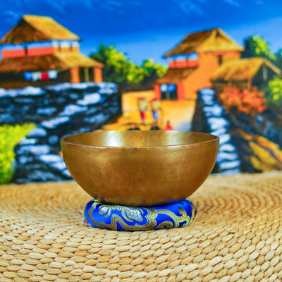 Handcrafted Himalayan singing bowl with a warm bronze-gold finish displayed on a decorative blue cushion for meditation practice.