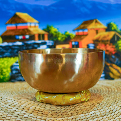 Side view of a handmade Himalayan singing bowl with a smooth bronze-gold finish displayed on a decorative yellow cushion.