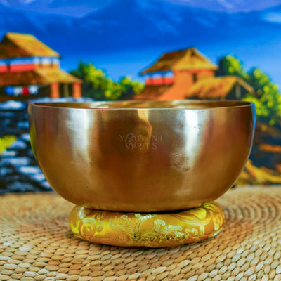 Side view of a handmade Himalayan singing bowl with a smooth bronze-gold finish displayed on a decorative yellow cushion.