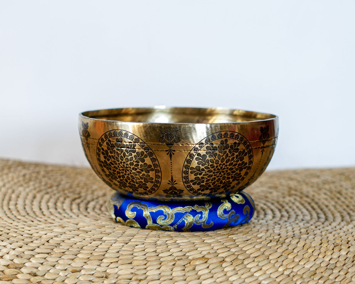 Golden Cosmos singing bowl with intricate floral and geometric engravings displayed on a blue brocade cushion.