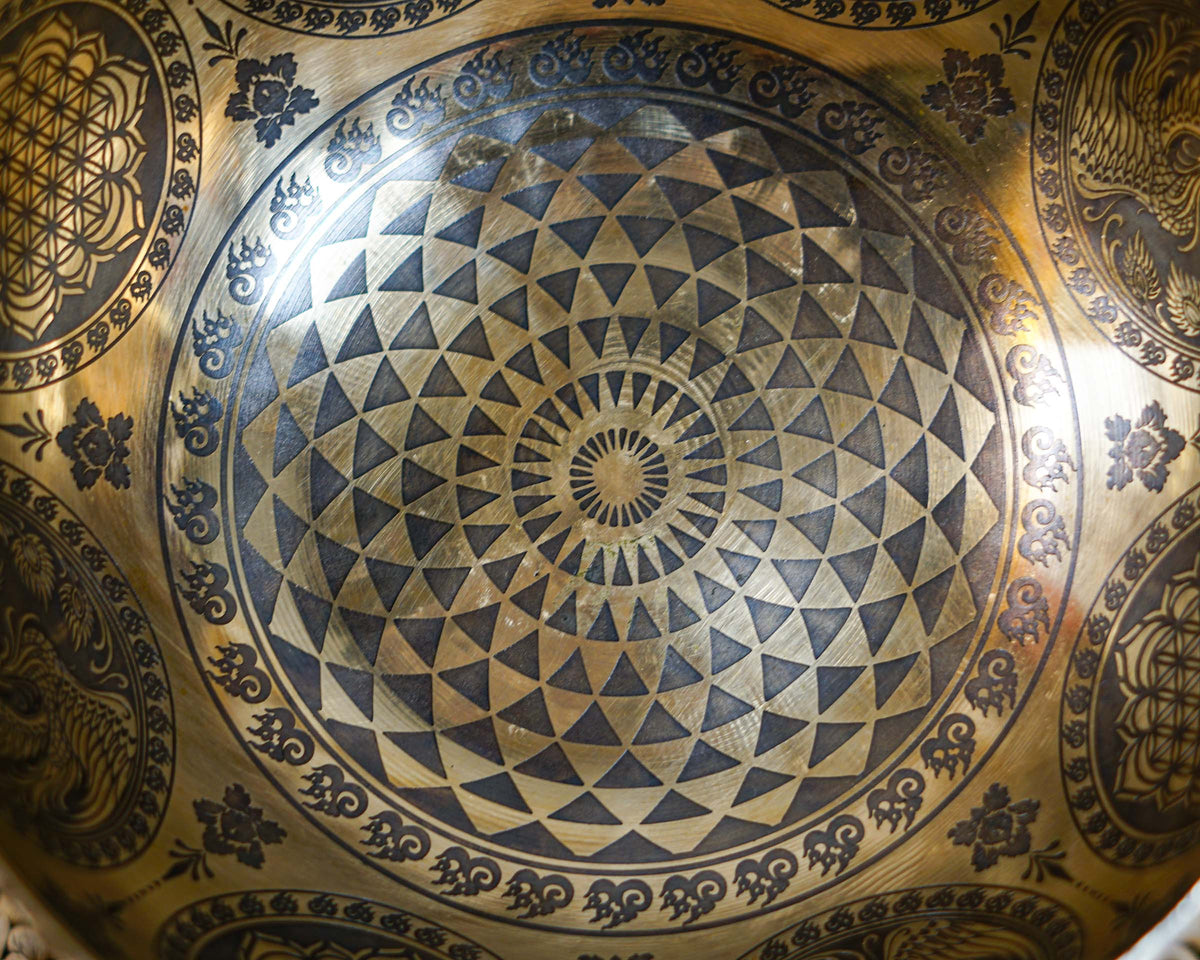 Close up of a Cosmos singing bowl featuring concentric triangular engravings and a radiating central geometric design.