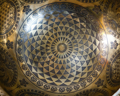 Close up of a Cosmos singing bowl featuring concentric triangular engravings and a radiating central geometric design.
