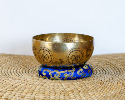Golden Turtle Design singing bowl with repeating engraved motifs displayed on a blue brocade cushion.