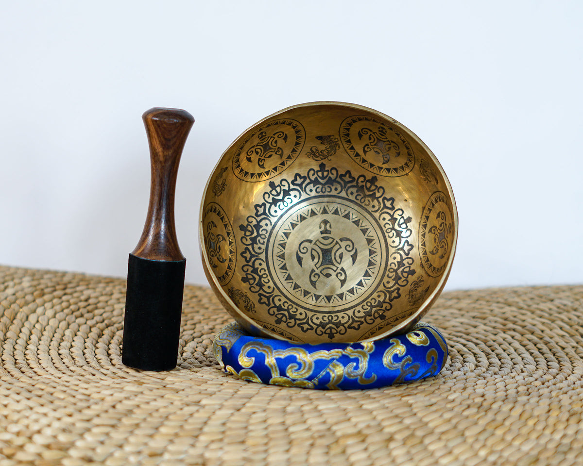 Turtle inspired engraved singing bowl displayed upright with a wooden mallet and blue cushion, showing the detailed interior artwork.