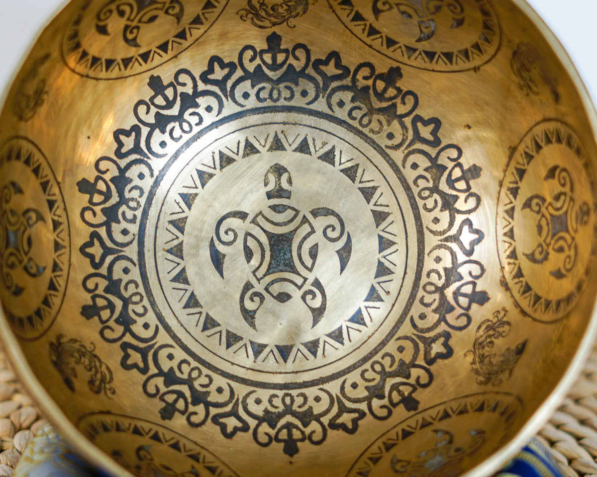 Close up of the golden singing bowl interior featuring a central turtle inspired engraving and intricate ornamental patterns.