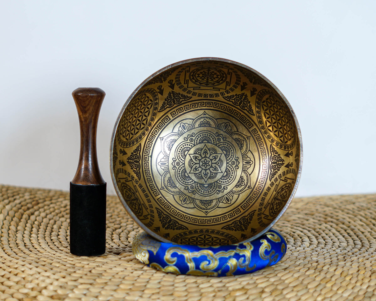 Floral Mandala singing bowl standing upright on a blue cushion beside a wooden mallet, showcasing its engraved interior design.