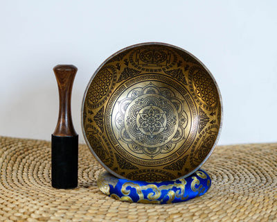 Floral Mandala singing bowl standing upright on a blue cushion beside a wooden mallet, showcasing its engraved interior design.