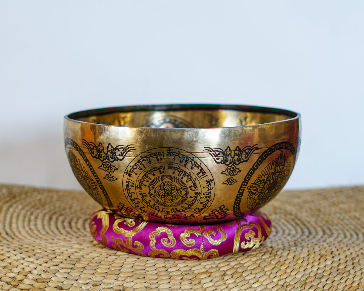 Golden Chengresi singing bowl displayed on a purple brocade cushion with intricate Tibetan Buddhist engravings