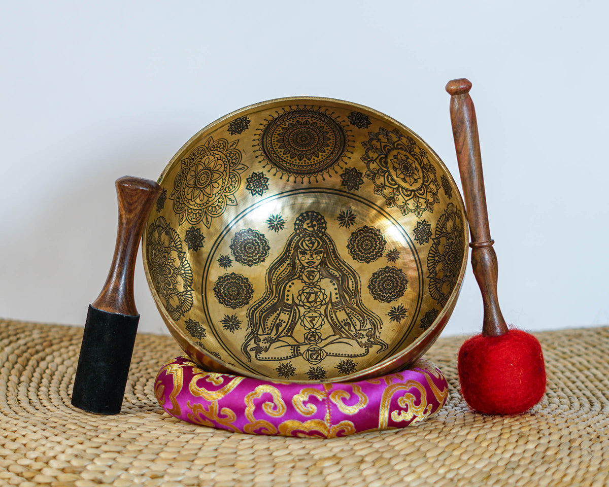 Golden Chakra Yogini singing bowl with engraved exterior motifs displayed on a purple brocade cushion