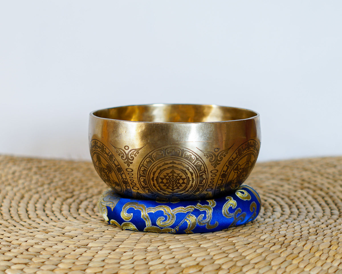 Tree of Life singing bowl displayed upright on a blue cushion with a suede mallet, showing the engraved tree design inside the bowl.