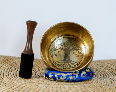 Golden Tree of Life singing bowl with decorative geometric and mandala inspired engravings displayed on a blue brocade cushion.