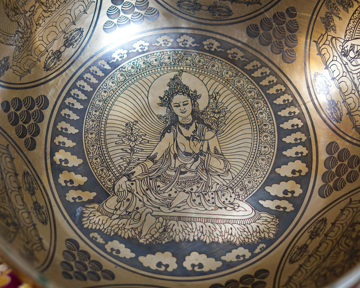Close up of Green Tara engraved inside a golden bronze tone singing bowl with lotus throne and decorative cloud patterns