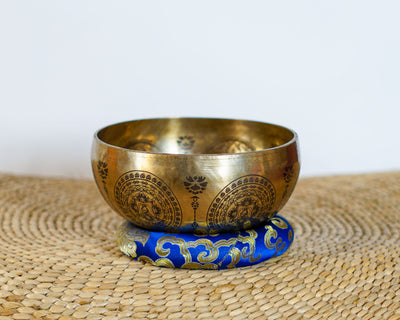Golden Green Tara singing bowl with intricate exterior engravings displayed on a blue brocade cushion.