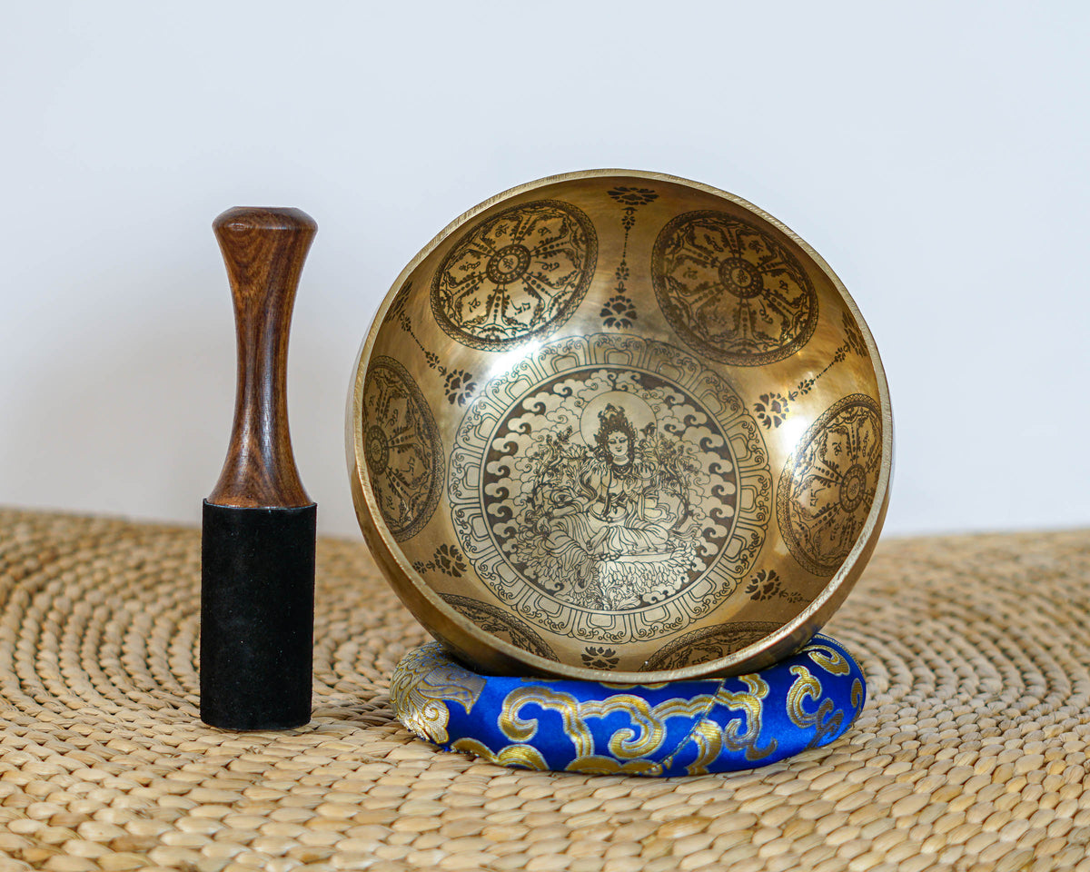Green Tara singing bowl displayed upright with a wooden mallet, showing the central deity engraving and decorative circular patterns.