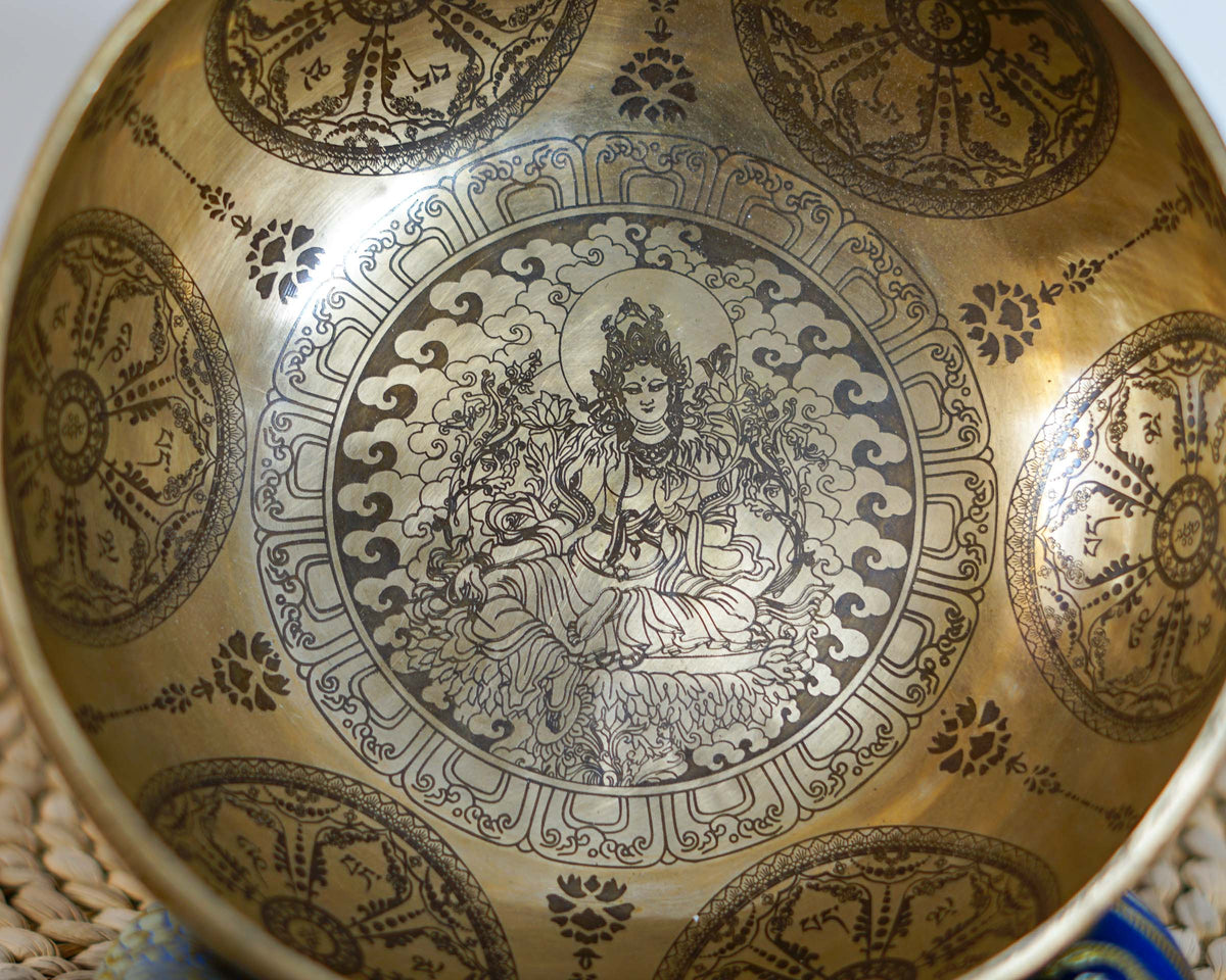Close up of Green Tara engraved inside a golden singing bowl, seated on a lotus throne and surrounded by decorative cloud motifs.