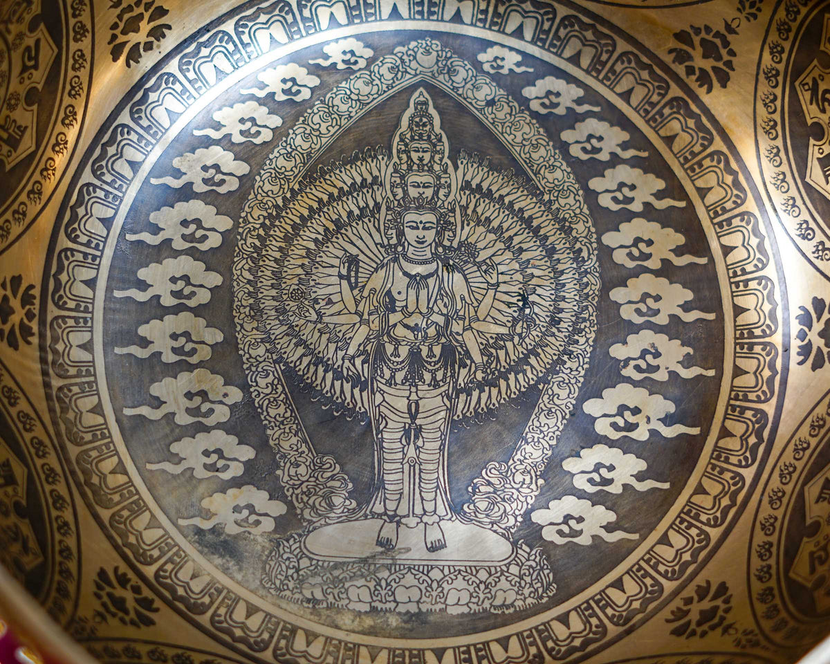 Close up of Avalokiteshvara with multiple arms and faces engraved inside a golden singing bowl.