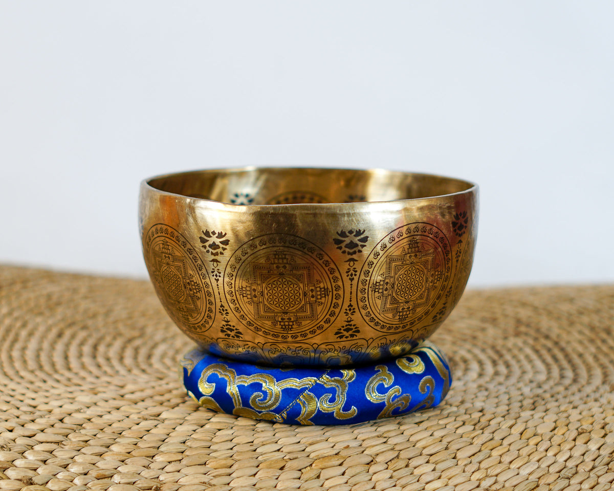 Golden Thousand Armed Avalokiteshvara singing bowl displayed on a blue brocade cushion with detailed exterior engravings.