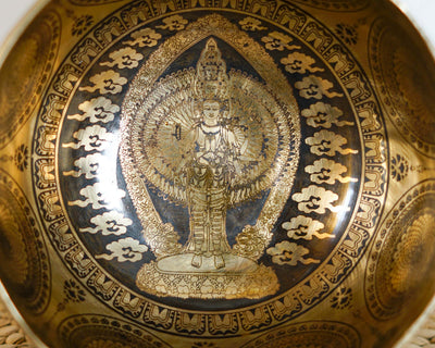 Close up of Thousand Armed Avalokiteshvara engraved inside a golden singing bowl with decorative cloud motifs.