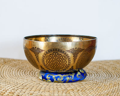 Golden Zambala singing bowl displayed on a blue brocade cushion, showcasing its engraved exterior and traditional design.
