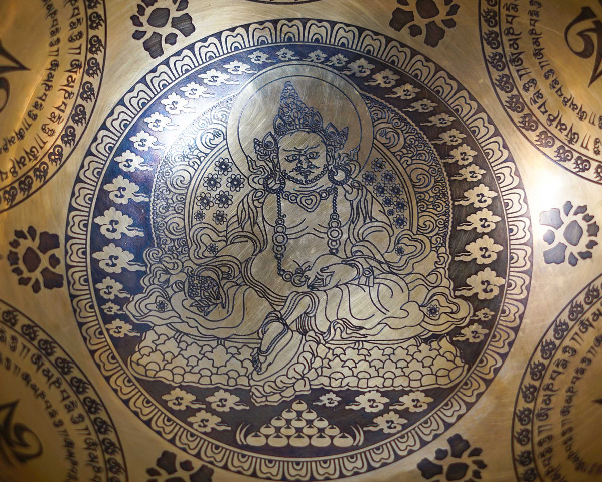 Close up of Zambala engraved inside a golden singing bowl with detailed Buddhist motifs and decorative cloud patterns.