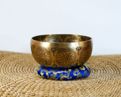 Golden Mahakala singing bowl resting on a blue brocade cushion, showing its engraved exterior and traditional ornamental details.
