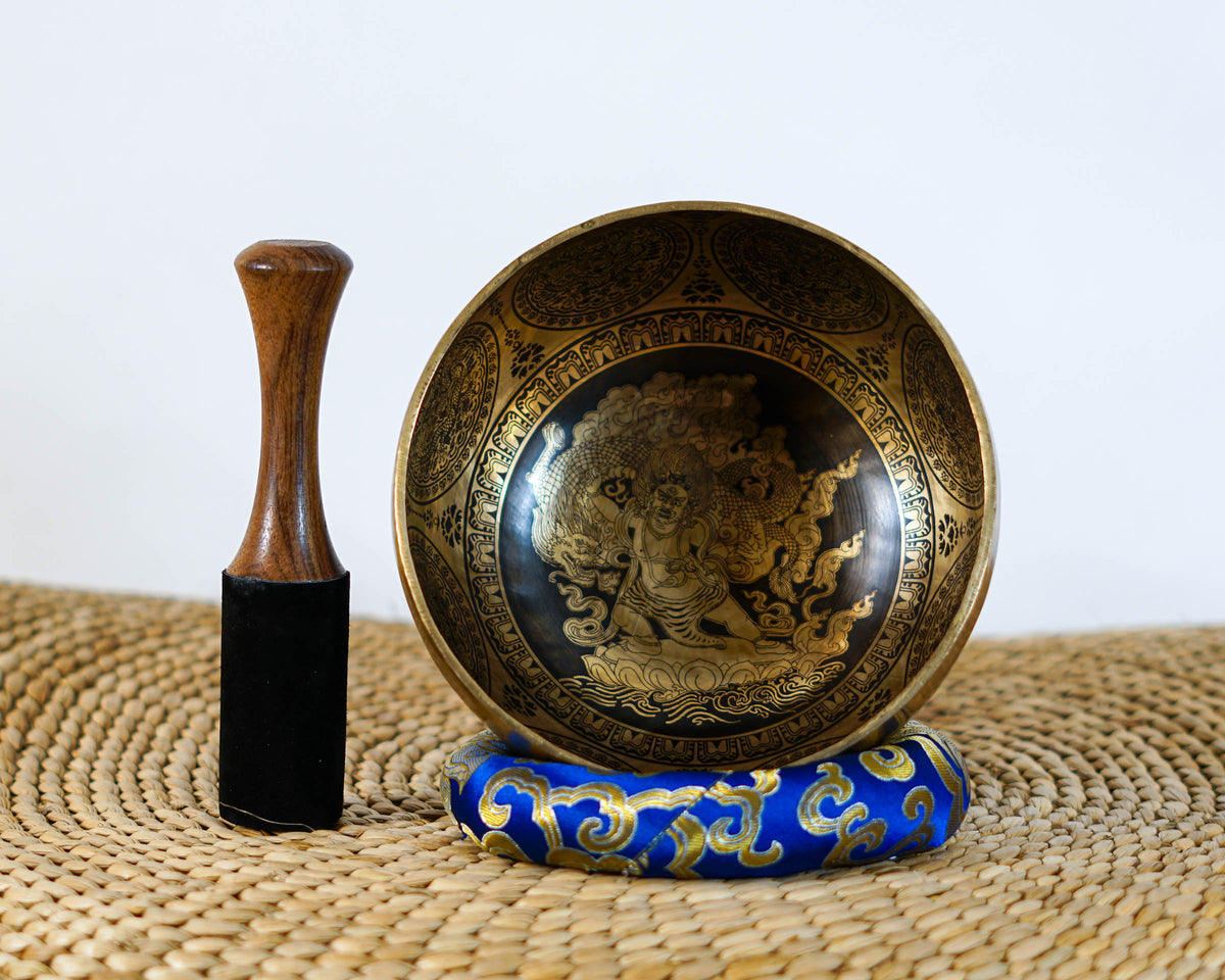 Mahakala engraved singing bowl displayed upright on a blue cushion with a wooden mallet, highlighting the detailed interior artwork.